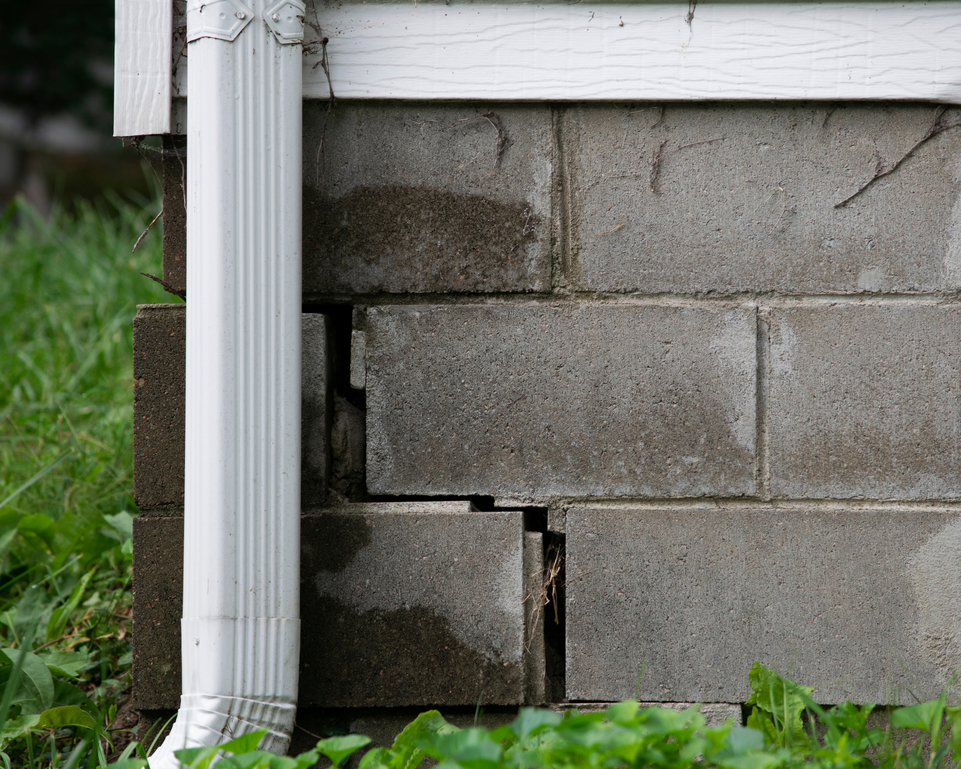 Cracked cinder block foundation with a white downspout. Water stains indicate a leak.