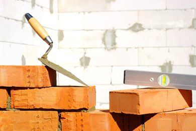 Bricks being laid with a trowel and level, on a wall under construction.