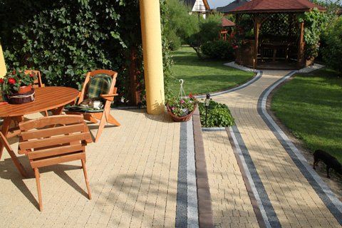 Patio with wooden table and chairs, leading to a gazebo via a paved pathway through a green yard.