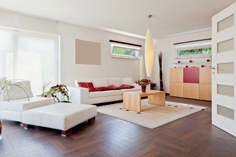 Modern living room with white furniture, wooden floors, and a minimalist aesthetic. Red accents pop against the neutral palette.