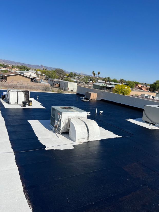 View from rooftop, showing freshly applied black sealant, white borders around equipment, and buildings under a blue sky.
