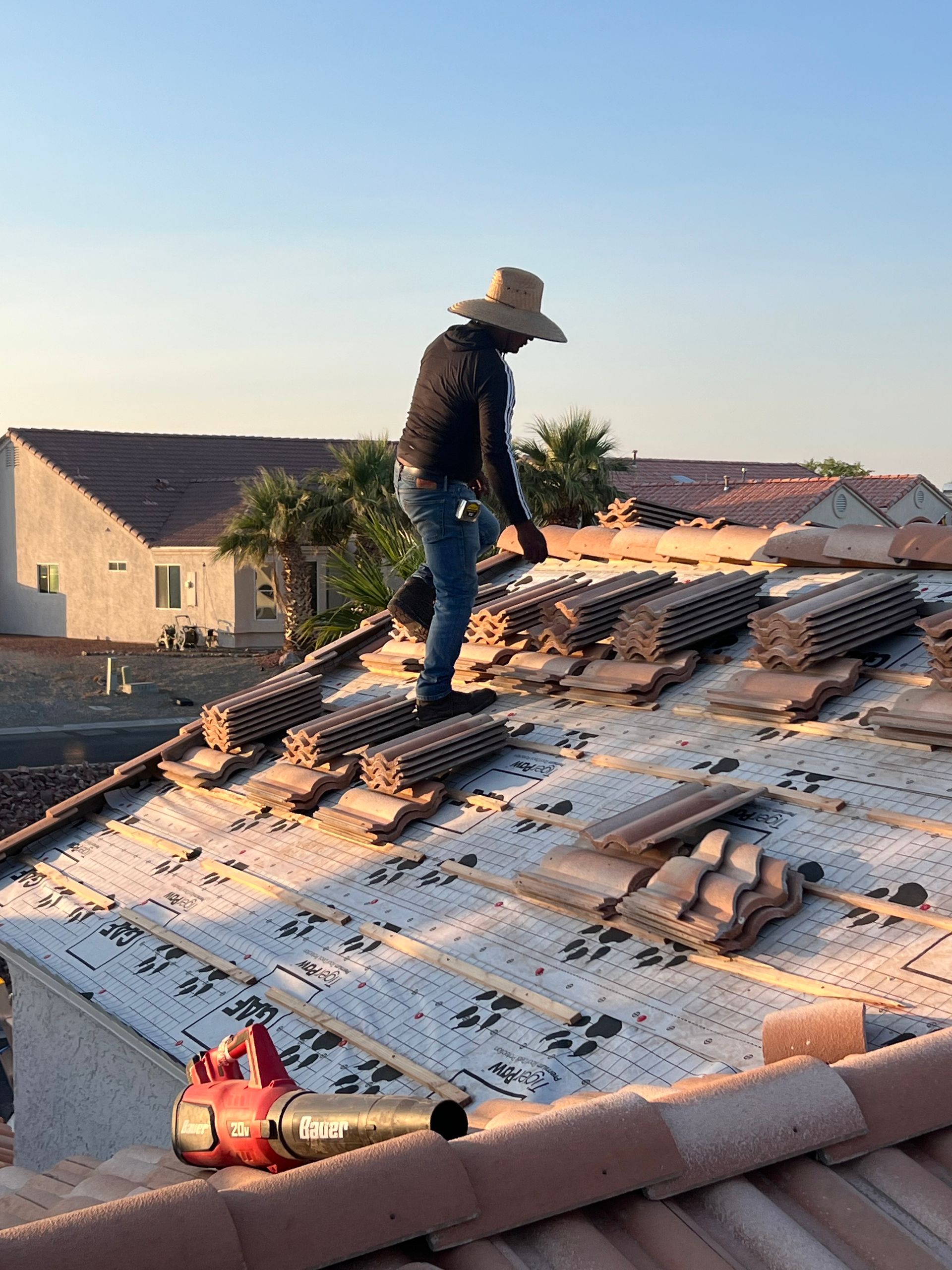 Roofer on a rooftop wearing a straw hat. Installing tiles, blue jeans, sunny outdoor setting.