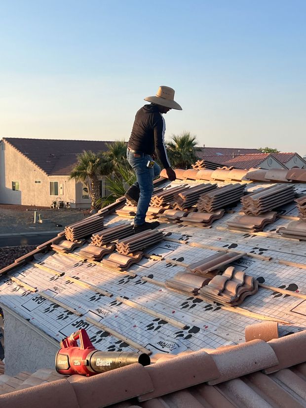 Roofer on a rooftop wearing a straw hat. Installing tiles, blue jeans, sunny outdoor setting.