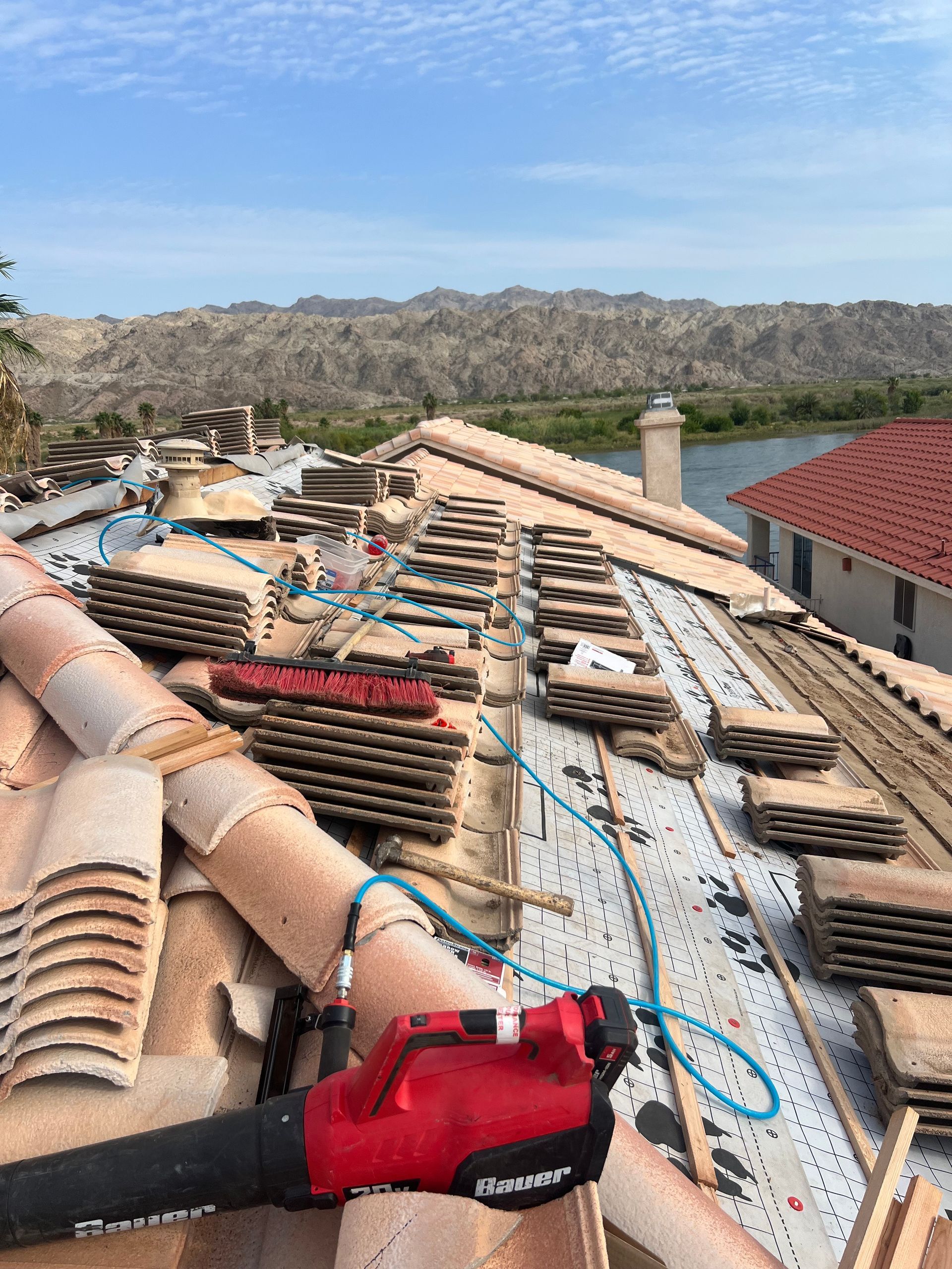 Roof under construction with stacks of tiles, tools, and a scenic mountain background.