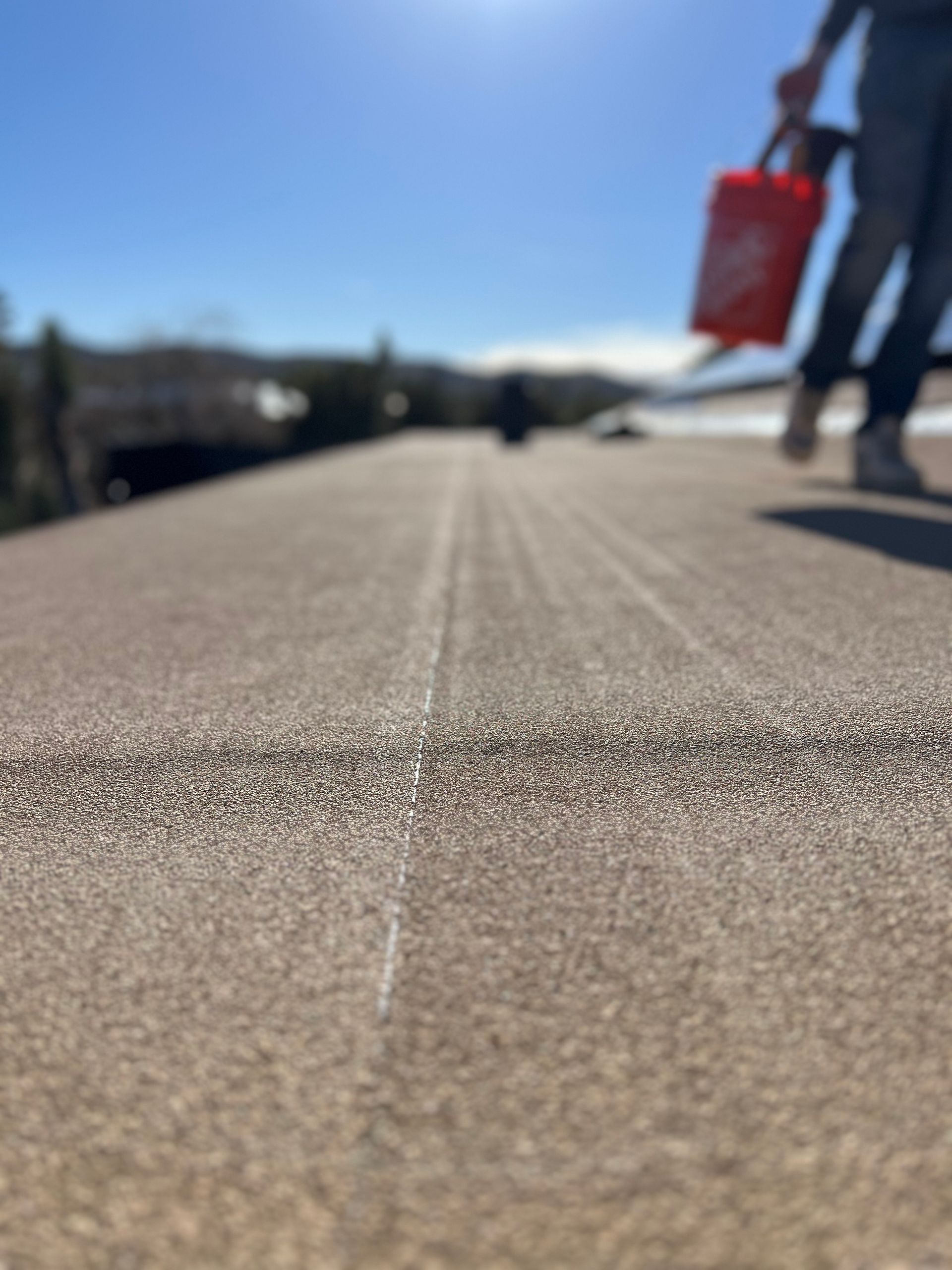 Person on rooftop, carrying bag, walking over gravel surface with white line. Clear, sunny day.