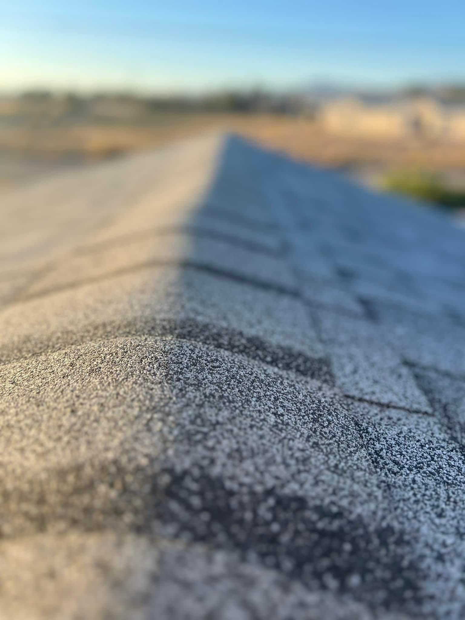 Close-up of a gray shingled roof with a clear sky and blurred desert landscape in the background.