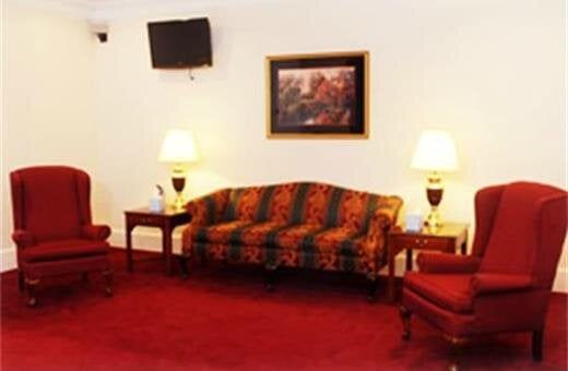A waiting area with red carpet, chairs, and sofa. Lamps flank the sofa under a framed artwork and TV.