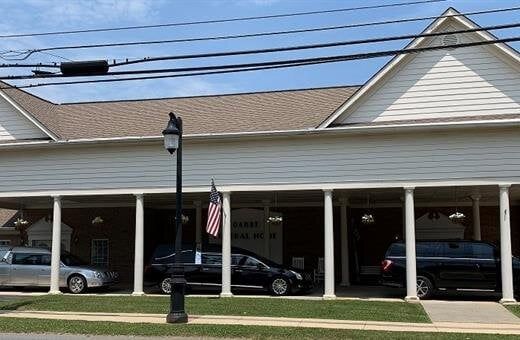 Funeral home exterior, white building with pillars, cars parked in front.