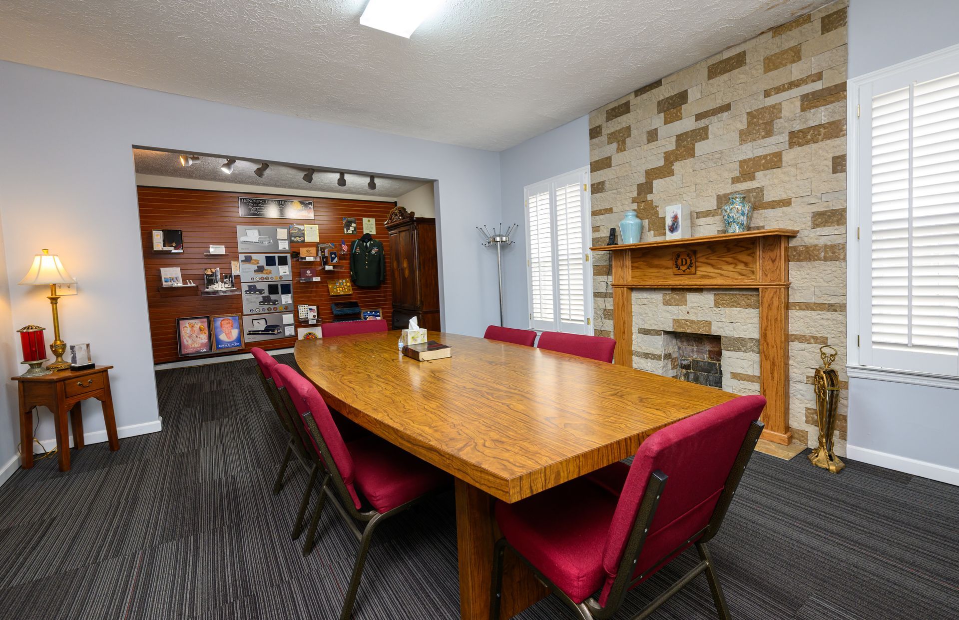 Funeral home showroom with three wooden caskets displayed on a red carpet, with urns and other merchandise on shelves in the background.