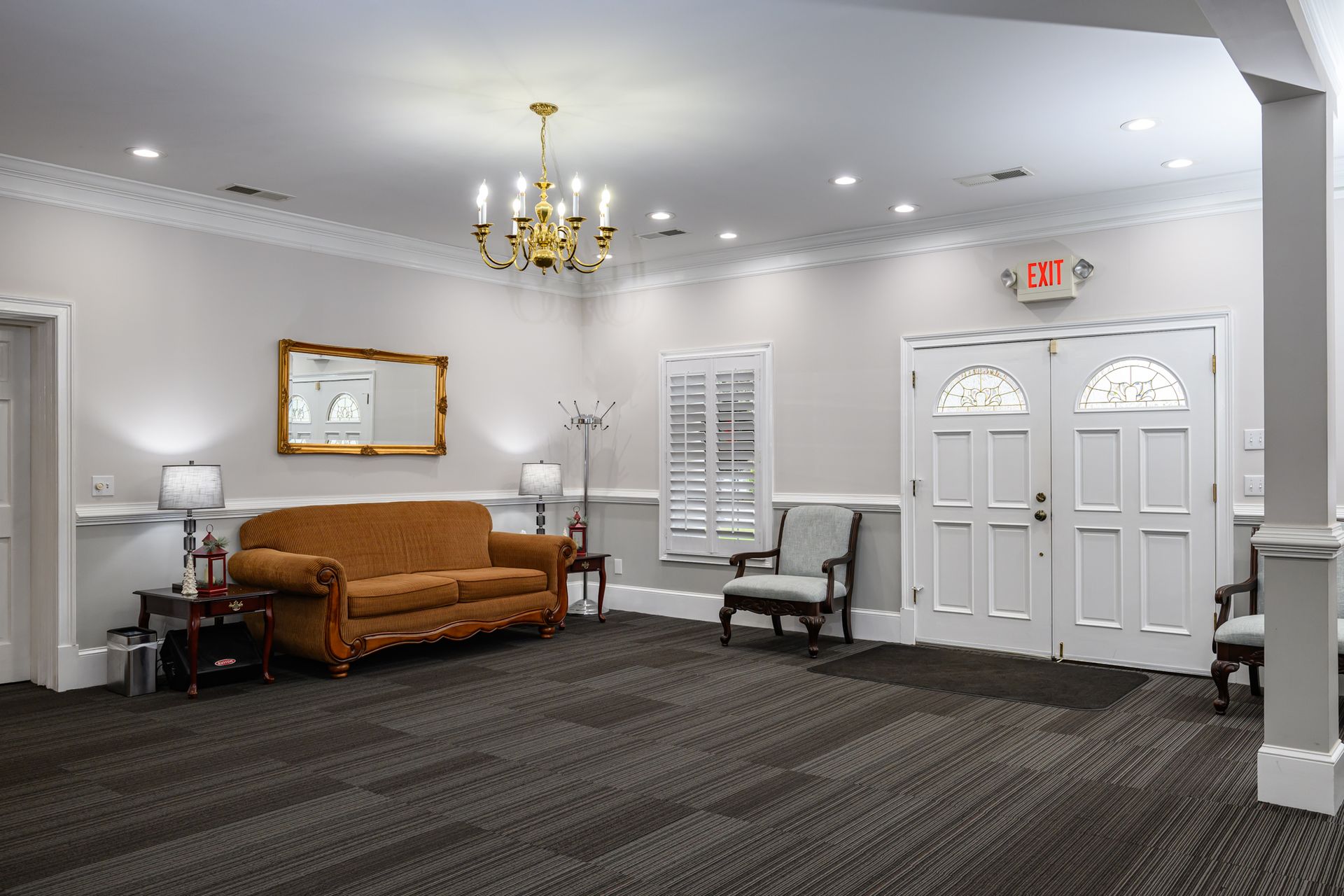 Funeral home waiting area with sofa, chair, lamps, and decorative window drapes.