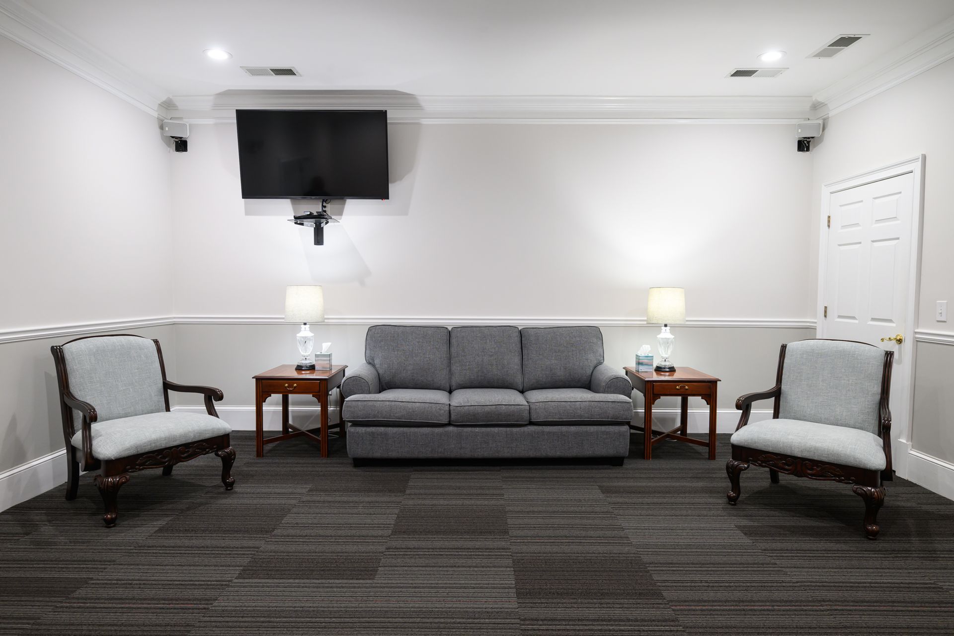 A waiting area with red carpet, chairs, and sofa. Lamps flank the sofa under a framed artwork and TV.