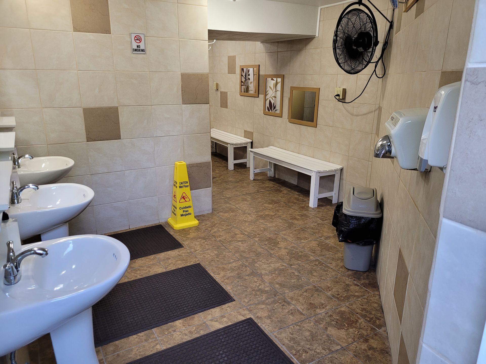 A bathroom with sinks , benches , and a yellow wet floor sign.