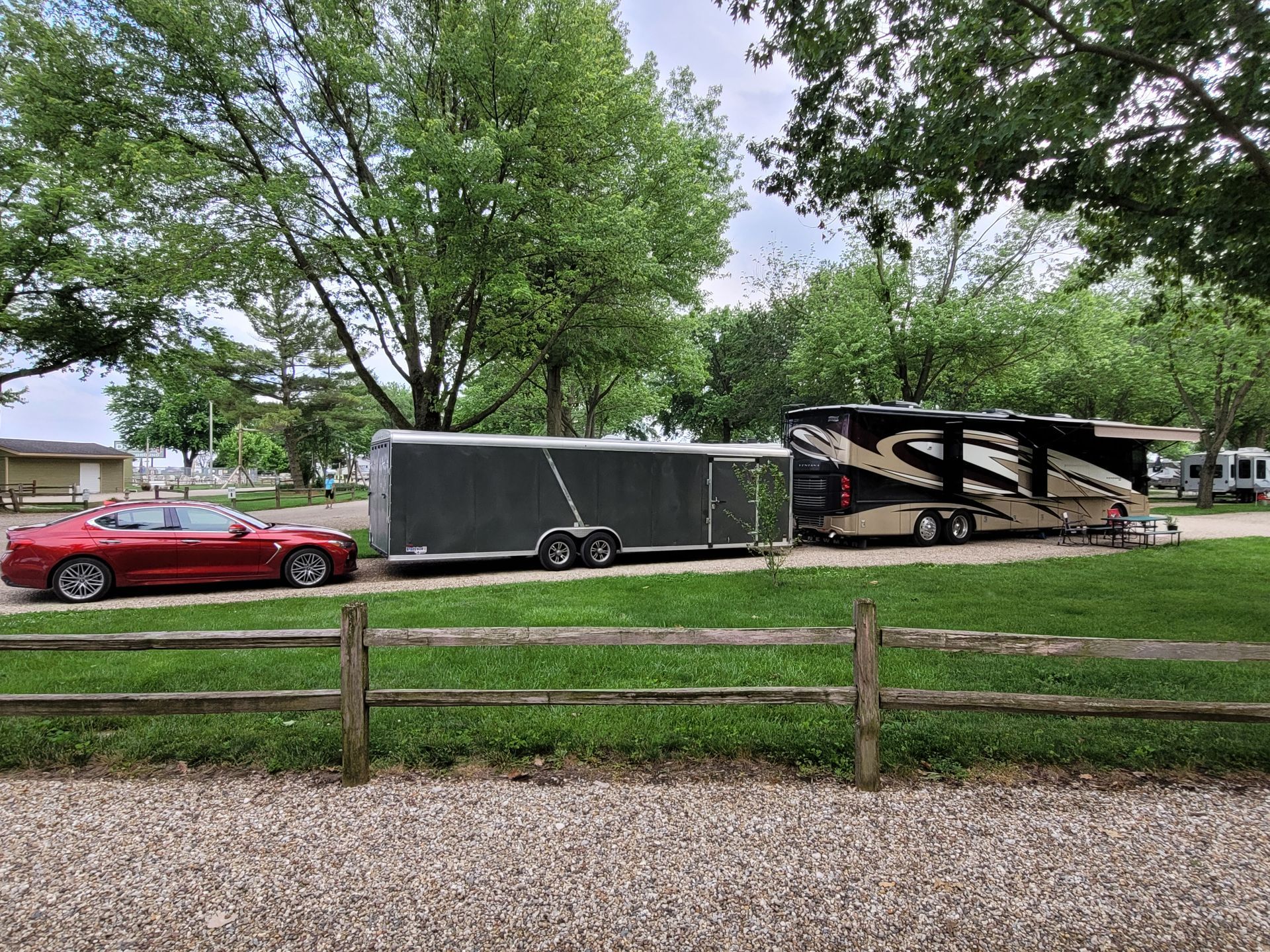 A red car is parked next to a trailer that is pulling a rv.