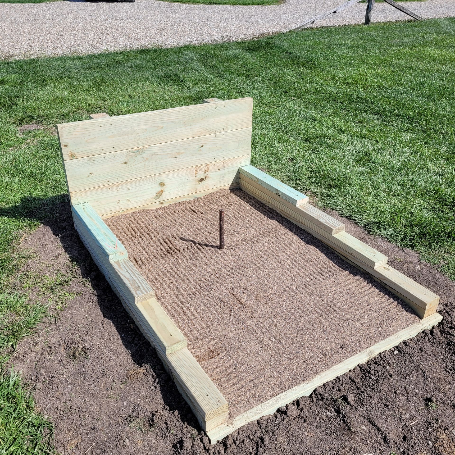 A wooden sandbox is sitting in the middle of a grassy field.