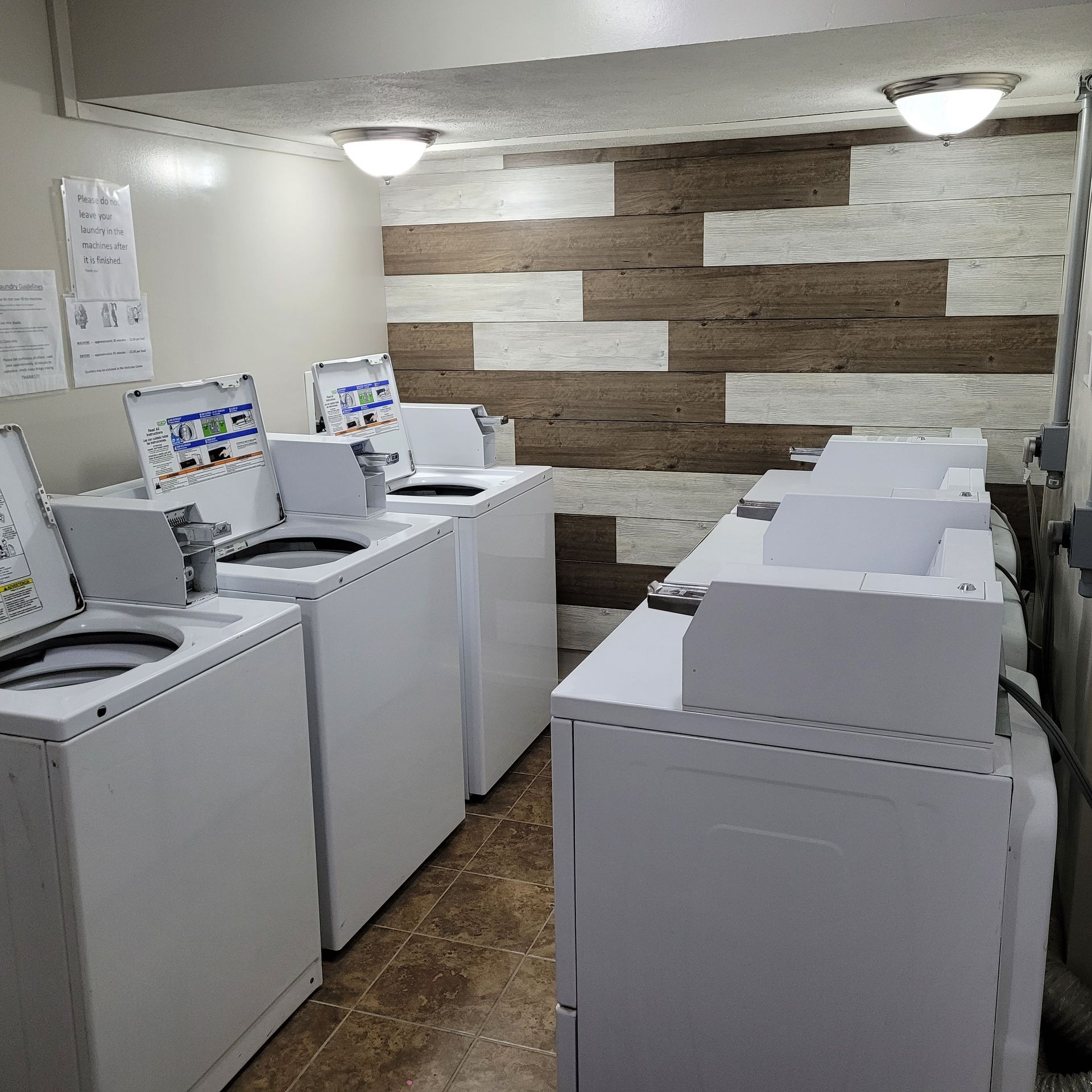 A row of washing machines in a laundromat with a wooden wall behind them.