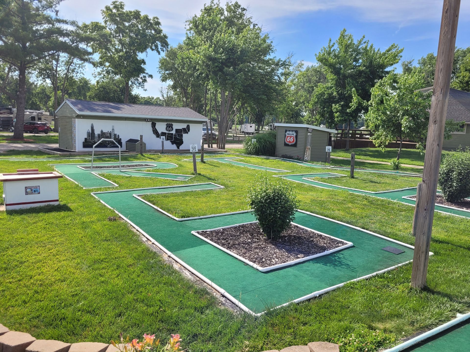 A mini golf course in a park with a white building in the background.