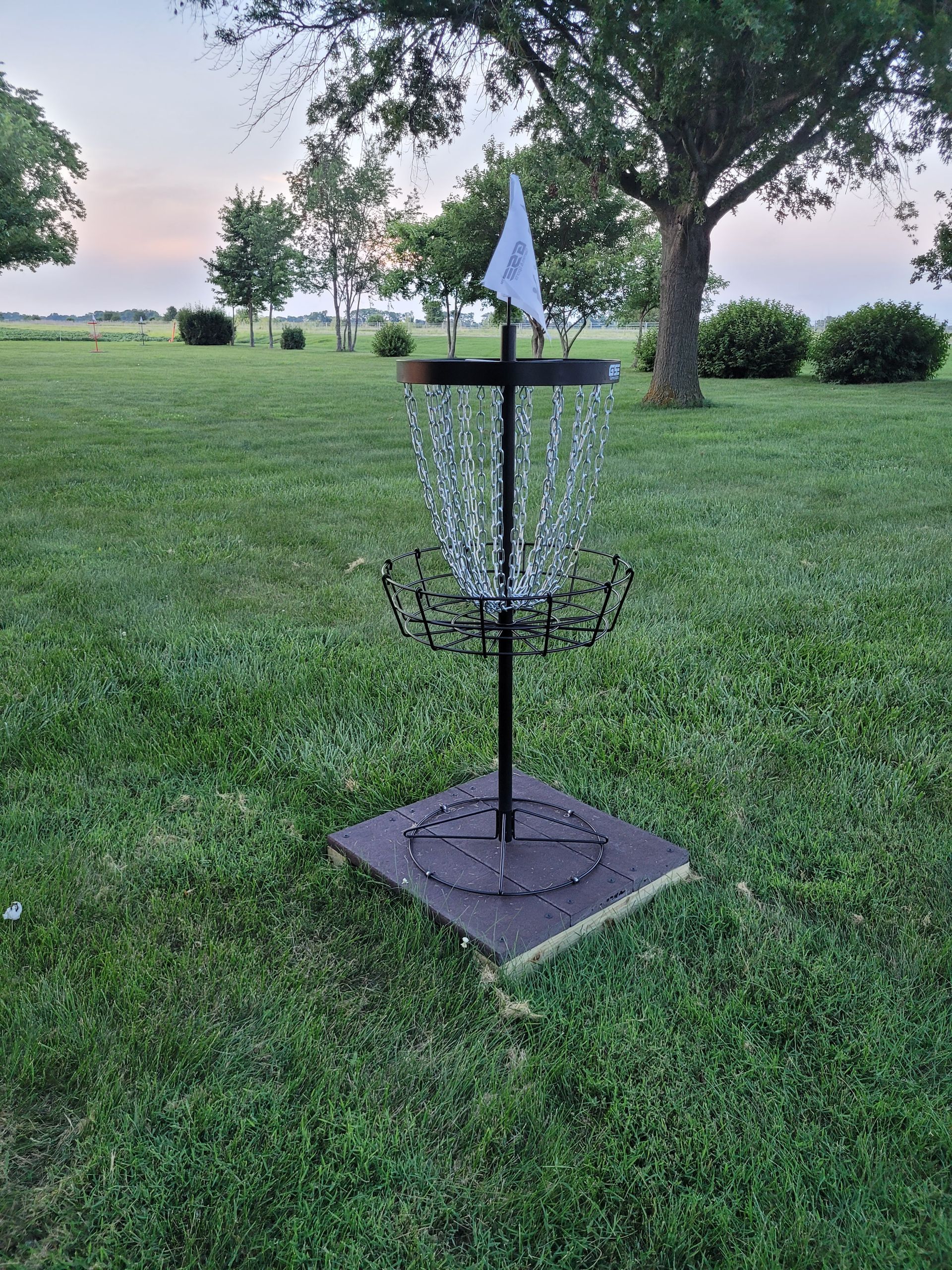 A frisbee golf basket is sitting in the middle of a lush green field.