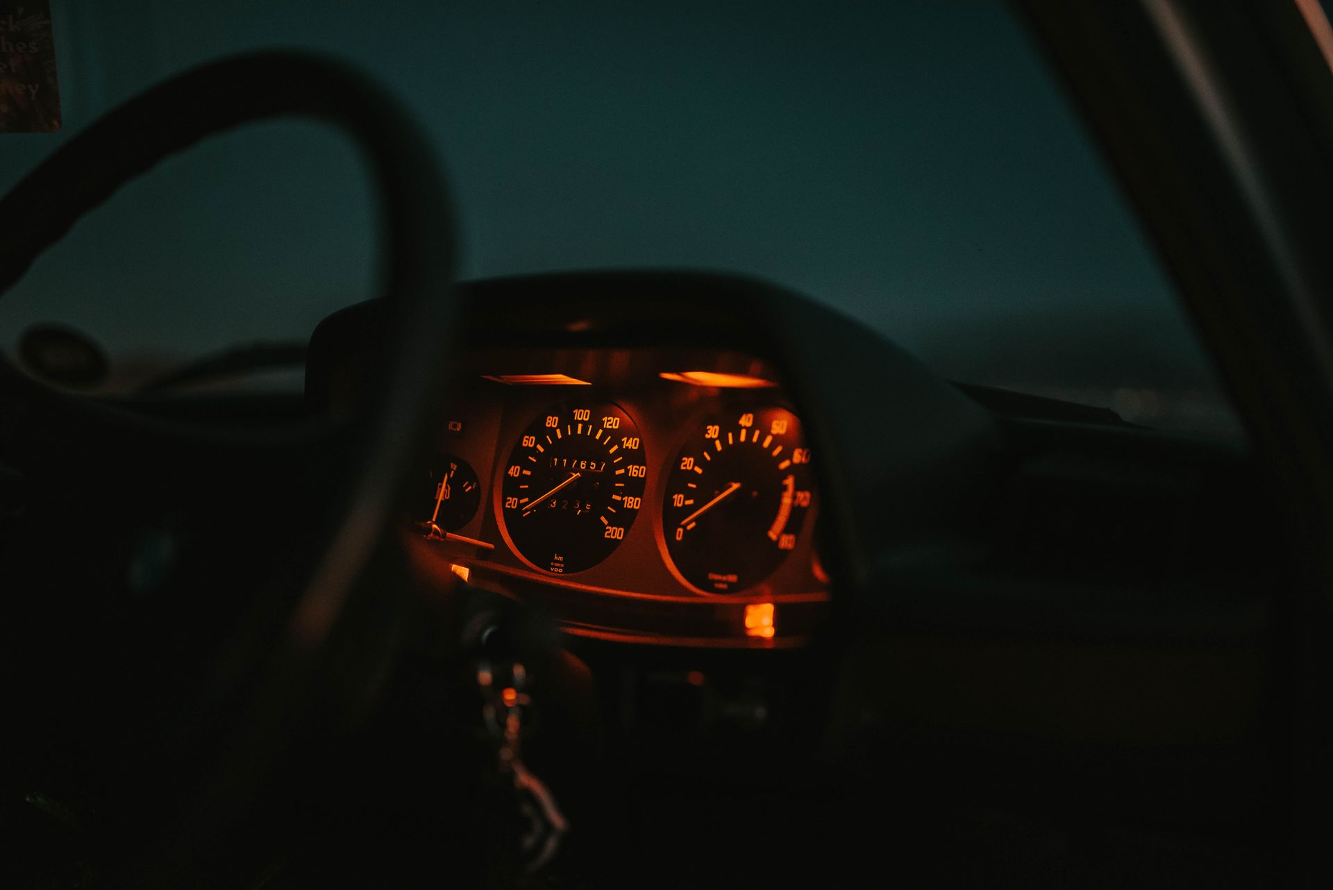 Illuminated car dashboard showing speedometer and other gauges glowing orange at night.
