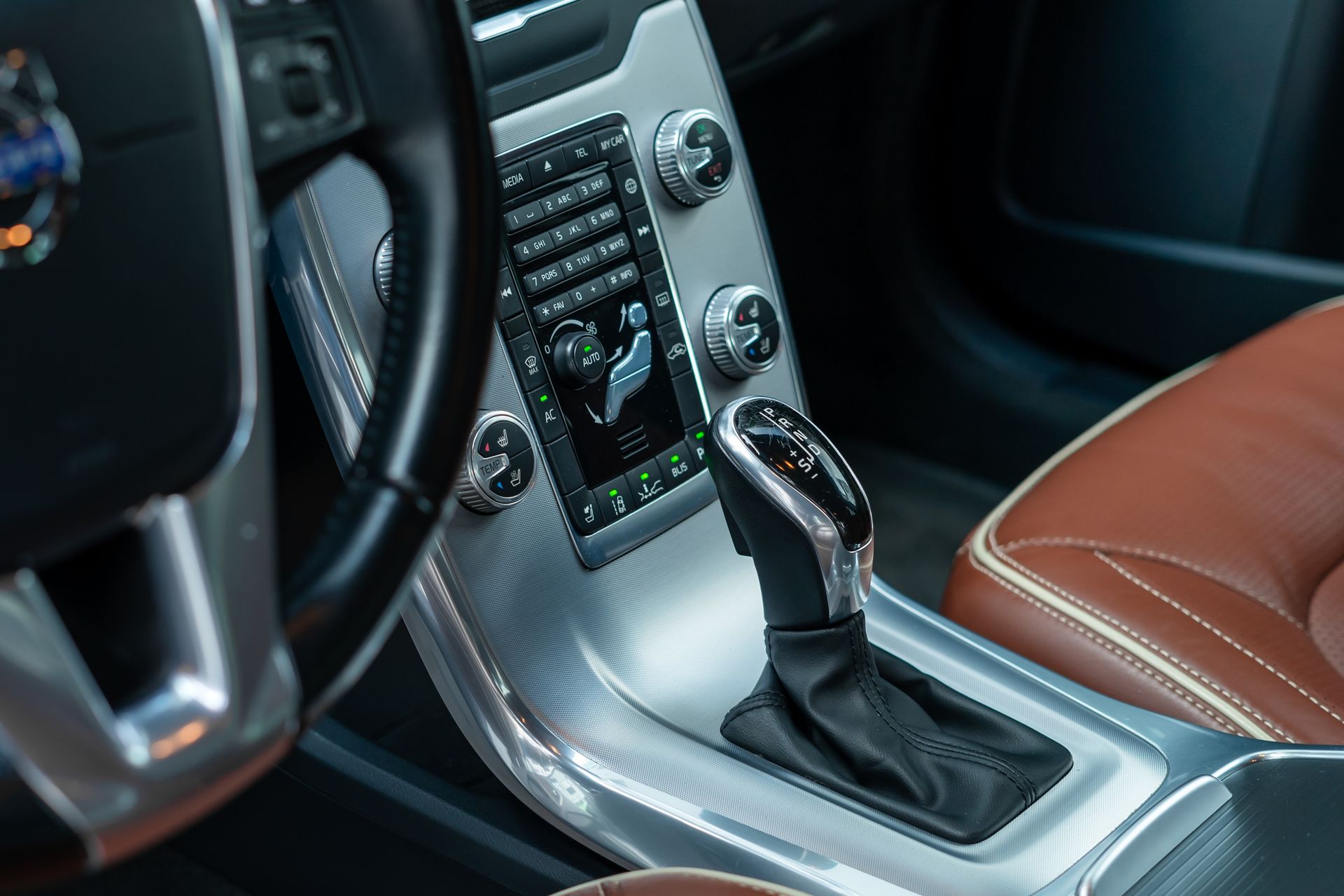 Car interior: leather seat, silver console with gear shift, dashboard with controls, and steering wheel.