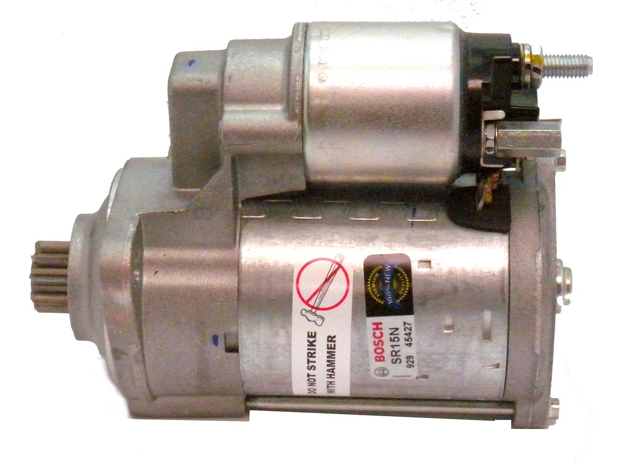 Car starter motor close-up, showing its metal body, solenoid, gear, bolts, and warning label .