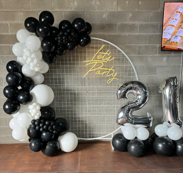 A balloon garland for 21st party with a neon sign that says let 's party