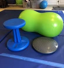 Blue and green exercise equipment on a blue mat. Includes a peanut ball, wobble cushion, and stool.