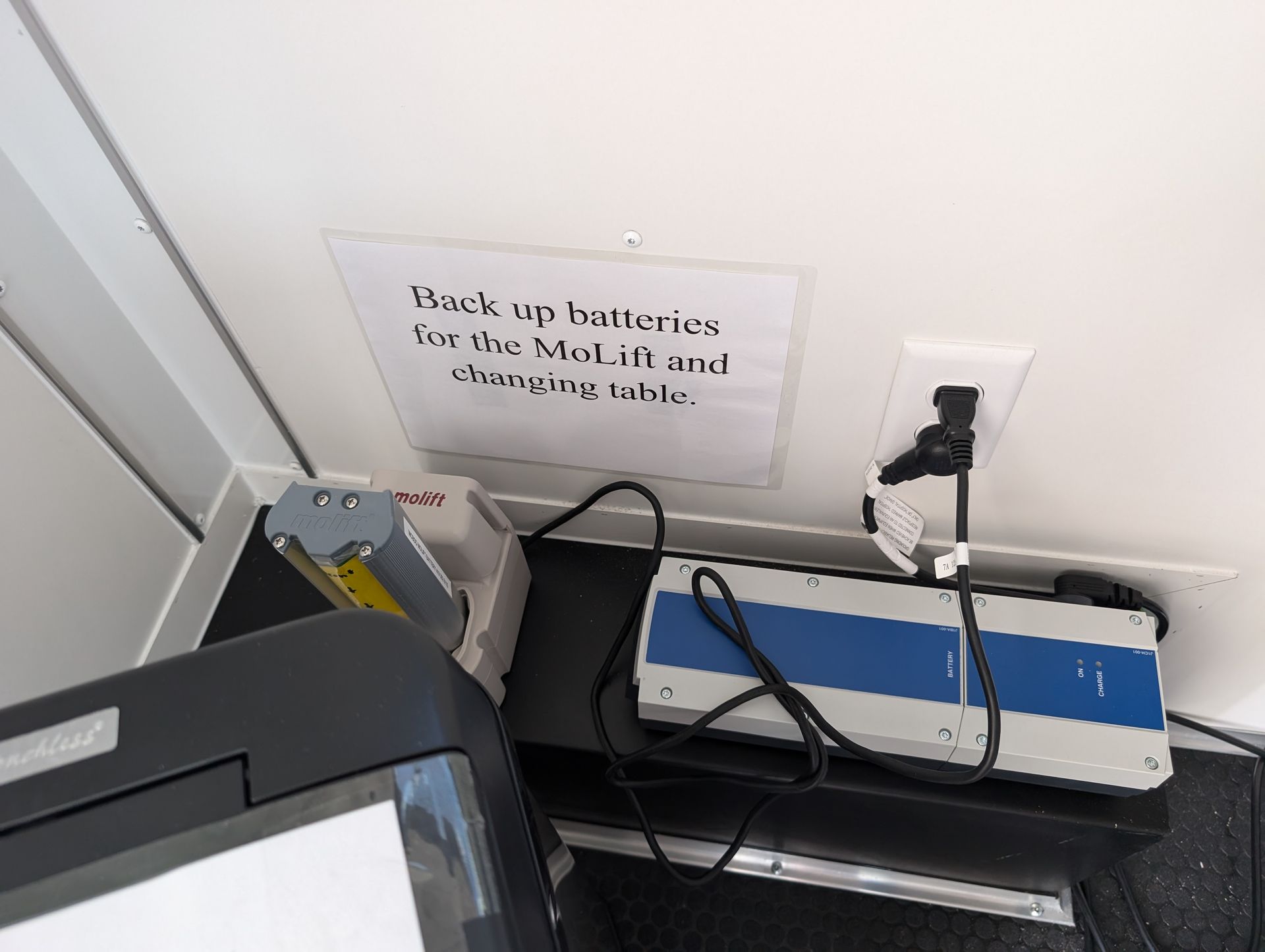 Battery back up on a table plugged into a wall outlet with a sign.