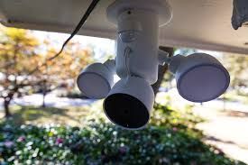 White security light with three adjustable heads, one with a black camera, mounted outdoors.