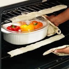 A casserole dish of stuffed peppers in an oven, with hands removing a dough strip.