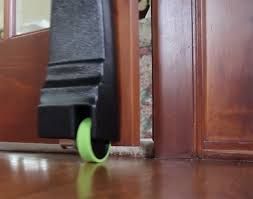Black wheeled furniture leg with green wheel, on wooden floor near a door.