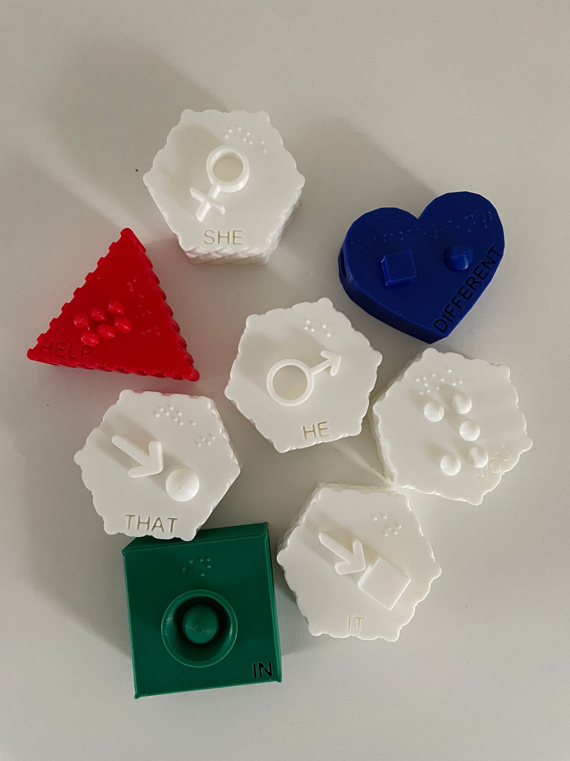 Seven colorful 3D printed shapes: a red triangle, a blue heart, and five white hexagons with various symbols.