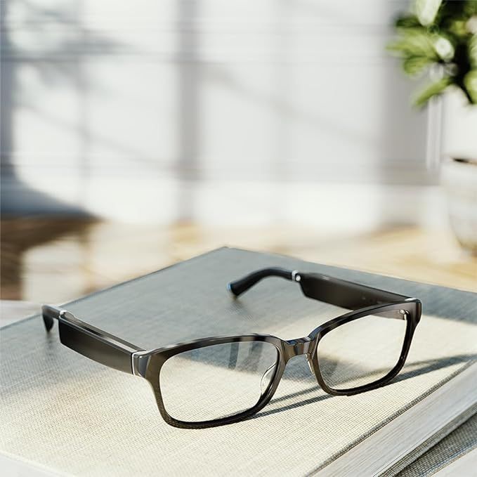 Black smart glasses resting on a book, sunny interior, blurred background.