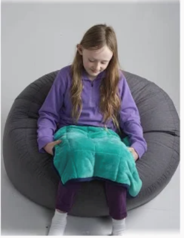 Girl sitting on beanbag, holding teal weighted blanket.