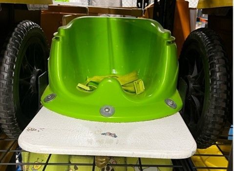 Green child's seat on a white platform, flanked by two black wheels.