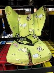 Green cushioned child's seating with cow and sheep print, including a chest strap, on a black metal shelf.