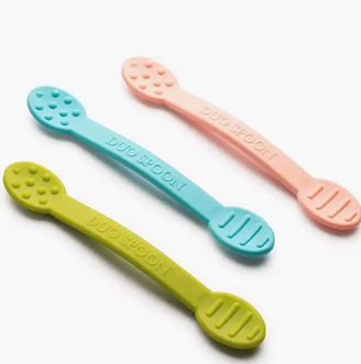 Three colorful baby spoons: green, blue, and pink, with textured spoon heads and handles labeled 