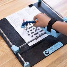 Person using a guided writing device, with a hand in a wrist brace, writing on paper. Black frame, light blue device.