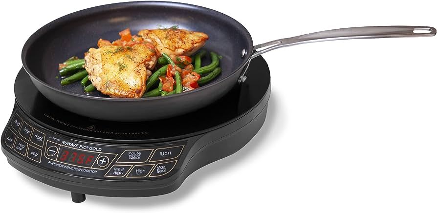 Frying pan with chicken and vegetables on a black induction cooktop.
