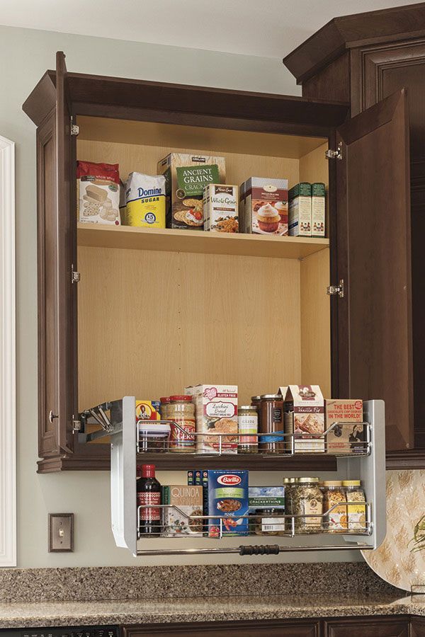 Opened dark wooden kitchen cabinet with pull-down shelf, filled with food items.
