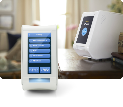 Two white home devices with screens displaying menus and time, on a wooden table indoors.