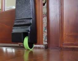 Black furniture leg with green caster rolling over a wood floor, stuck between two wood doorframes.