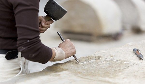 Ein Mann bearbeitet einen Stein mit Hammer und Meißel.