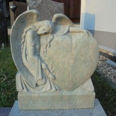 Eine Engelsstatue, die auf einem herzförmigen Grabstein sitzt.