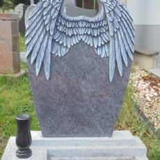 Auf einem Friedhof steht ein Grabstein mit eingeschnitzten Engelsflügeln.