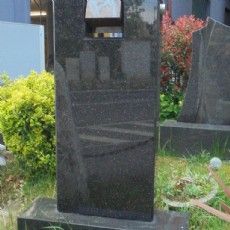 Ein Grabstein aus schwarzem Granit liegt im Gras auf einem Friedhof.