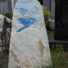 Ein großer weißer Stein mit einer blauen Bemalung liegt im Gras.