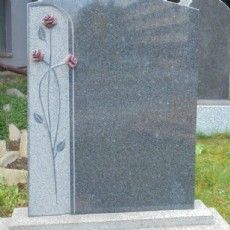 Auf einem Friedhof steht ein Grabstein mit eingemeißelten Rosen.