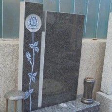 Ein Grabstein mit einer Blume darauf steht neben einer Vase.