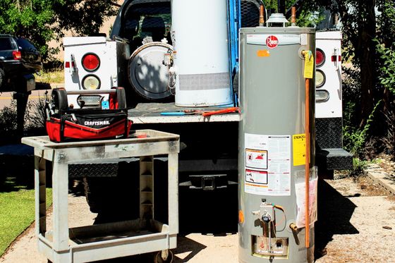 A plumber's truck with a new water heater next to it, tools, and a white cabinet.