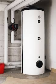 A tall, white cylindrical water heater in a basement next to pipes and a red bucket.